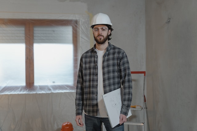 a contractor in a flannel shirt and white hard hat holding a floor plan